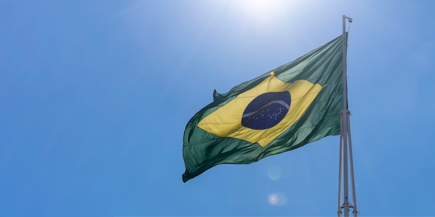 Bandera de Brasil ondeando en el cielo azul con rayos de sol Orden y progreso en portugués Brazilia