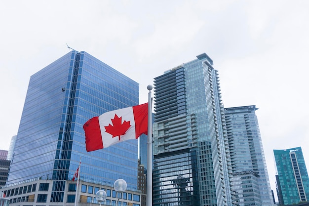 Bandera canadiense frente a un moderno edificio de cristal en Vancouver