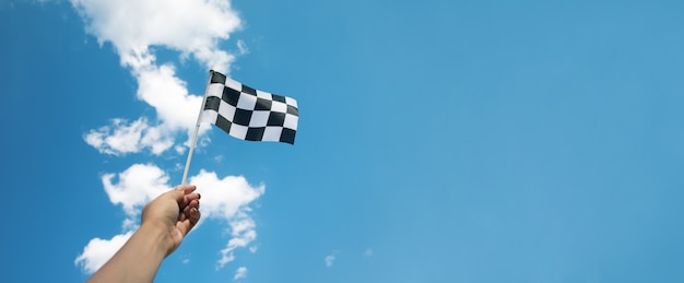 Bandera de carrera a cuadros en la mano sobre el cielo azul