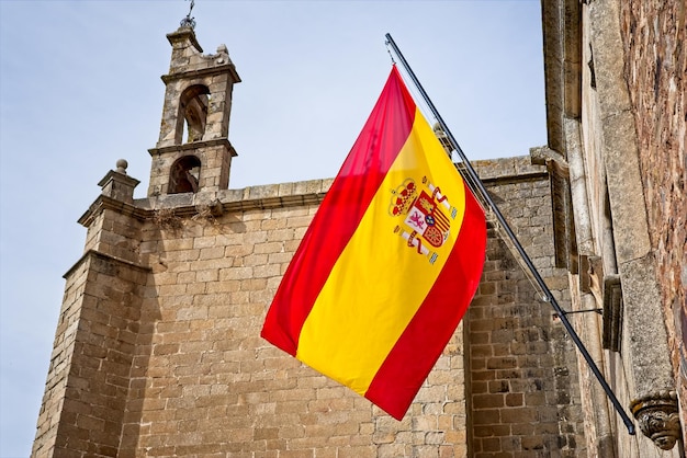 Foto bandera de españa frente a una antigua iglesia en cáceres