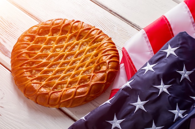 Bandera de Estados Unidos que pone al lado de la tarta. Producto de panadería cerca de banner brillante. Pastelería tradicional en mesa blanca. Sabor a patriotismo.