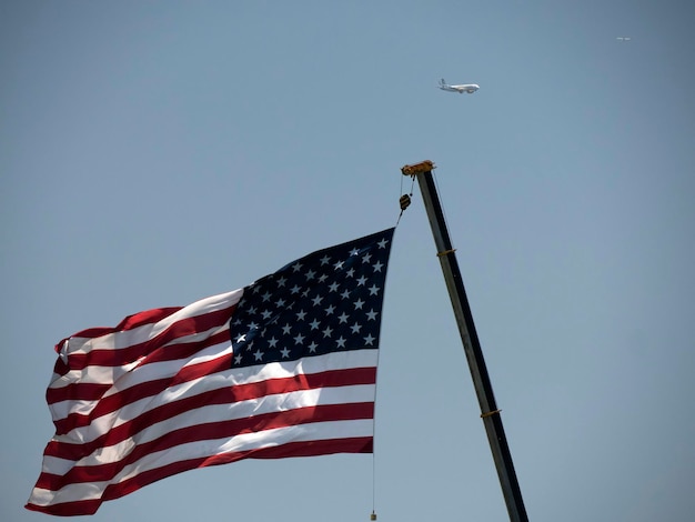 Bandera estadounidense contra un cielo azul claro y un avión