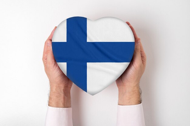 Bandera de Finlandia en una caja en forma de corazón en manos masculinas. Fondo blanco