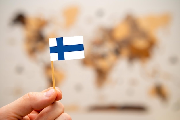 Bandera de Finlandia en la mano del hombre en el fondo del mapa mundial