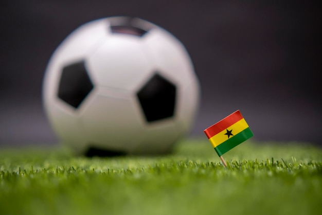 Bandera de Ghana y balón de fútbol en el campo de fútbol Balón blanco y negro clásico de fútbol en el fondo Competición deportiva La bandera nacional del país Césped verde fresco