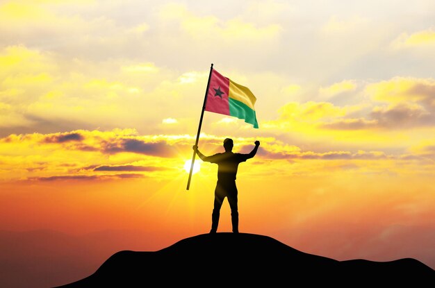 La bandera de Guinea-Bissau es ondeada por un hombre que celebra el éxito en la cima de una montaña