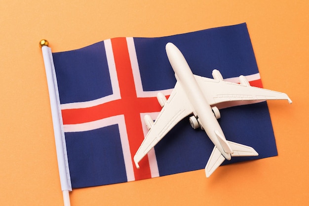 Bandera de Islandia y avión de juguete sobre fondo naranja, concepto de vuelo a Islandia, vista superior