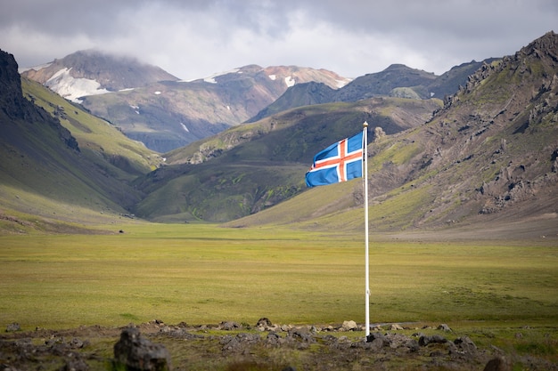 Bandera de Islandia contra el de verdes montañas y cielo azul.