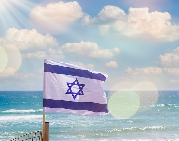 Bandera israelí al sol con cielo nublado y mar de fondo El concepto del día de la independencia de Israel Yom Haatzmaut Bandera de Israel con mástil ondeando en el viento Símbolos del estado nacional