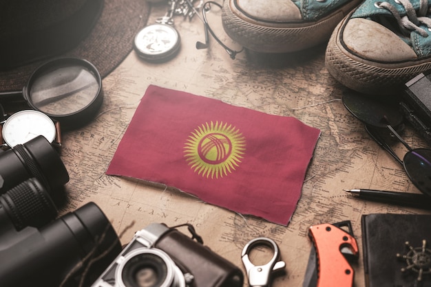 Bandera de Kirguistán entre los accesorios del viajero en el mapa antiguo vintage. Concepto de destino turístico.