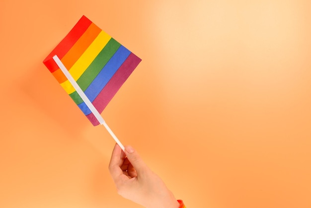 Bandera LGBT en mano de mujer sobre fondo naranja Copiar espacio