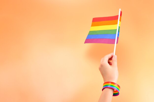 Bandera LGBT en mano de mujer sobre fondo naranja. Copie el espacio.