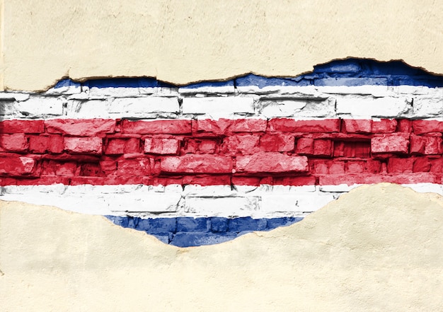 Bandera nacional de Costa Rica sobre un fondo de ladrillo. Pared de ladrillo con yeso, fondo o textura parcialmente destruidos.