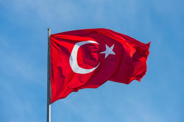 Bandera nacional de Turquía en un asta de bandera que agita contra un cielo azul