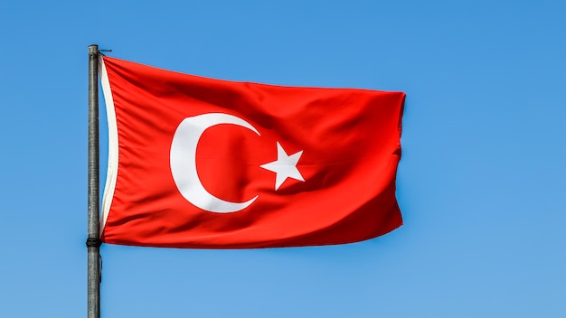 Bandera nacional de Turquía en un asta de bandera en el viento contra un fondo de cielo azul.