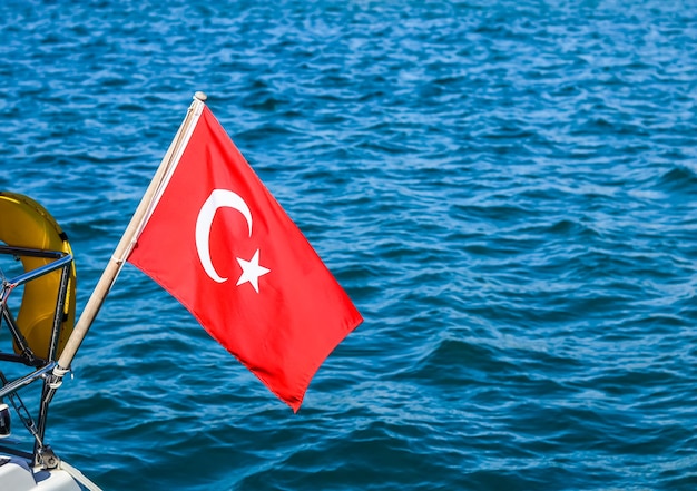 Foto bandera nacional de turquía en un asta de bandera en el viento contra un fondo de mar azul.