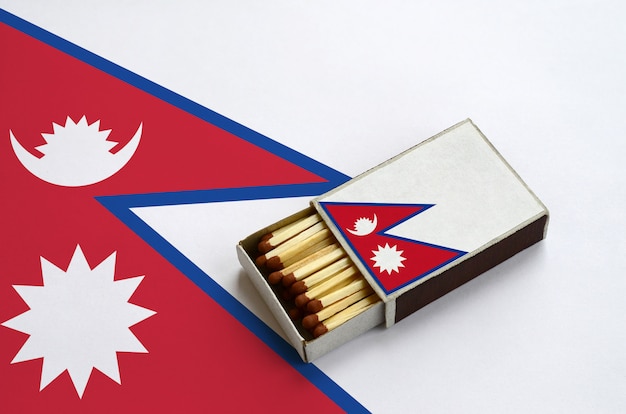 La bandera de Nepal se muestra en una caja de fósforos abierta, que está llena de fósforos y se encuentra en una bandera grande