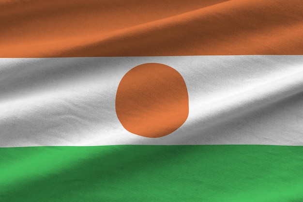 Bandera de Níger con grandes pliegues ondeando de cerca bajo la luz del estudio en el interior Los símbolos y colores oficiales en la pancarta