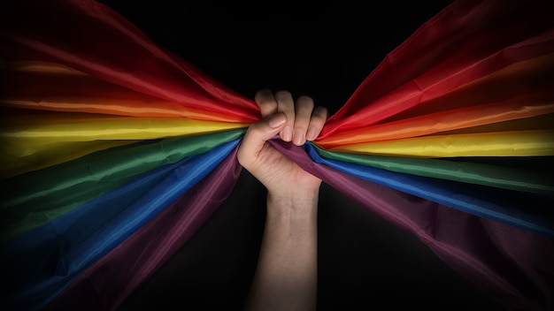 Bandera del orgullo LGBTQ. Lesbianas Gay Bi sexsual Transgénero Queer. Orgullo homosexual Bandera del arco iris en mano gay. fondo negro. Representa el símbolo de libertad, paz, igualdad y amor. Concepto LGBTQ.