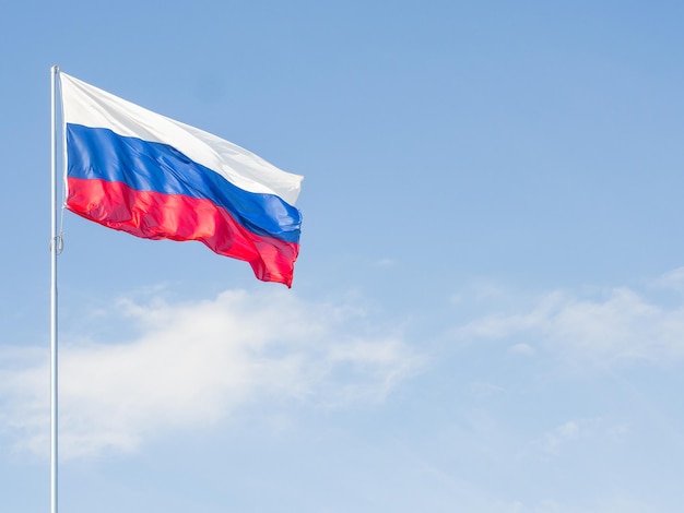 La bandera de Rusia ondeando en el viento contra un cielo azul con nubes