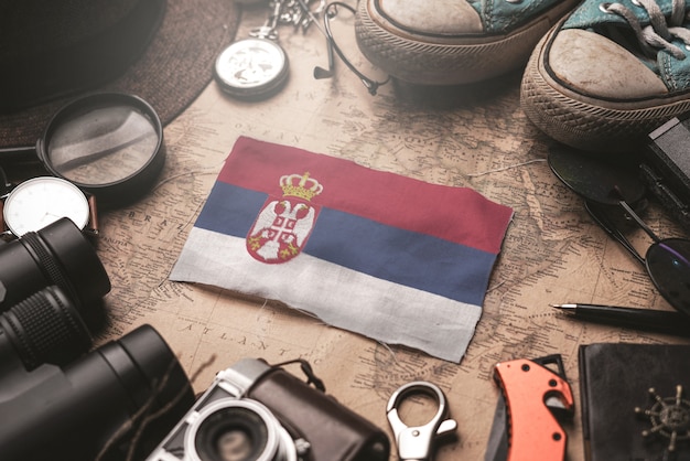 Bandera de Serbia entre los accesorios del viajero en el viejo mapa vintage. Concepto de destino turístico.