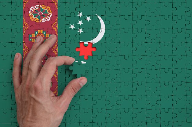 La bandera de Turkmenistán está representada en un rompecabezas, que la mano del hombre completa para doblar