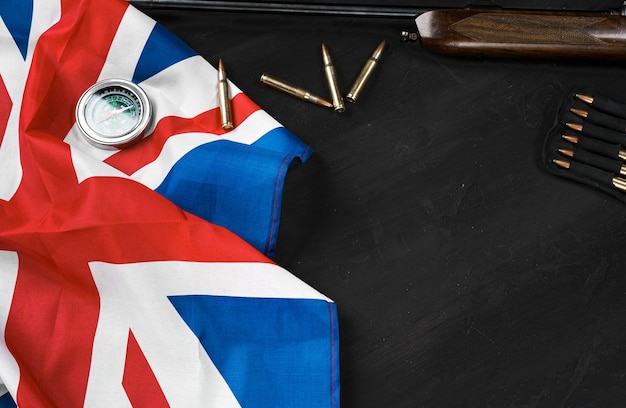 Bandera Union Jack con rifle y cartuchos sobre fondo negro