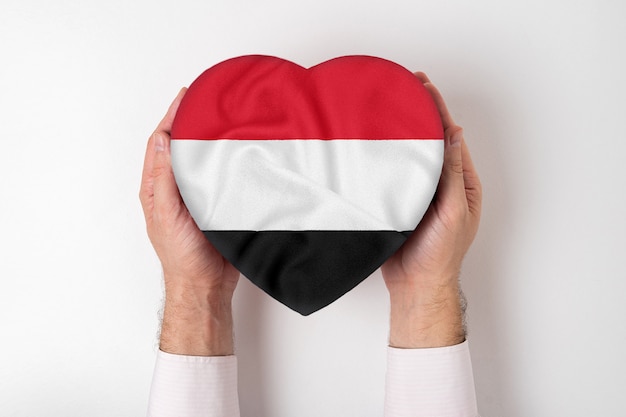 Bandera de Yemen en una caja en forma de corazón en manos masculinas.