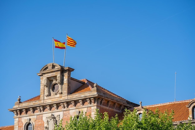 Banderas españolas y catalanas en un poste ondeando en la parte superior del edificio histórico en Barcelona España Cielo azul y árboles verdes en un parque