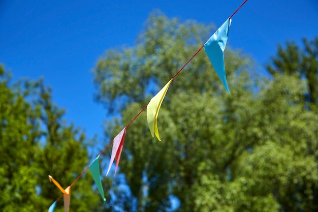 Banderas del festival de papel triangular multicolor en cielo azul y árboles verdes