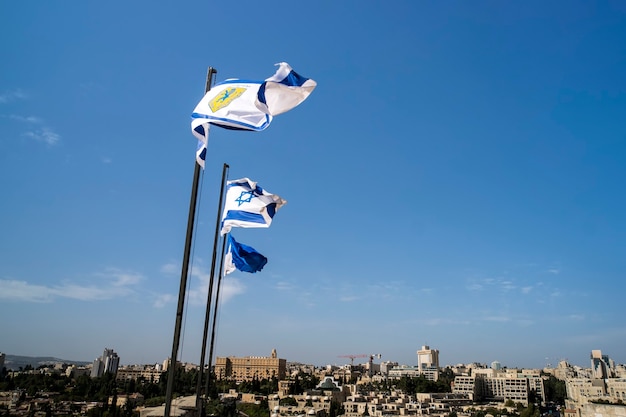 Banderas de Israel y Jerusalén en las murallas de la ciudad vieja de Jerusalén contra el cielo azul con nubes blancas en la luz del soleado verano.