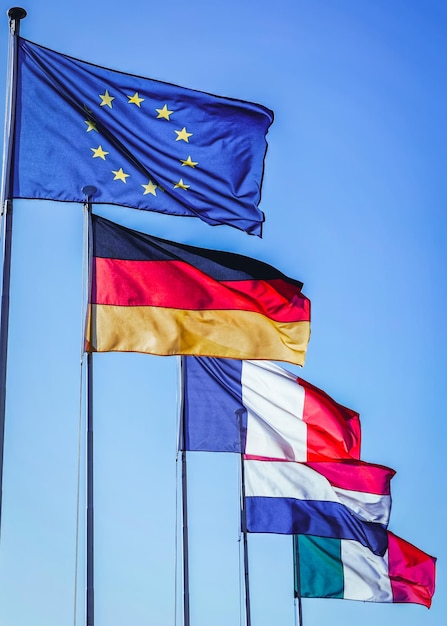 Foto banderas de la ue, alemania, francia, italia. estrellas de la unión europea, banderas nacionales alemanas, francesas e italianas ondeando al viento. fondo de cielo azul. visión patriótica.