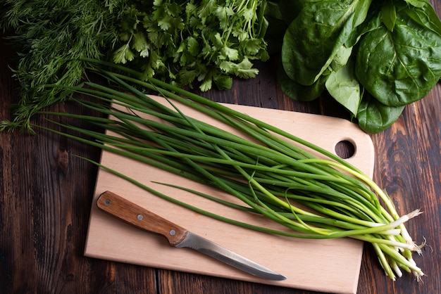 Bando de cebolas verdes frescas com verdes em uma placa de corte em um fundo de madeira, estilo rústico, conceito de comida vegetariana útil, close-up.