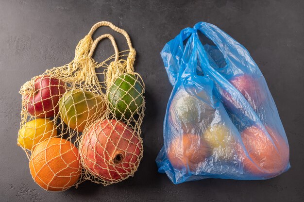 Bando de frutas orgânicas misturadas, vegetais e verdes em um saco de barbante e plástico em fundo escuro.