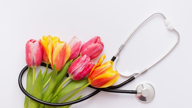 Bando de tulipas cor de rosa e estetoscópio sobre fundo branco. dia nacional do médico. feliz dia da enfermeira.