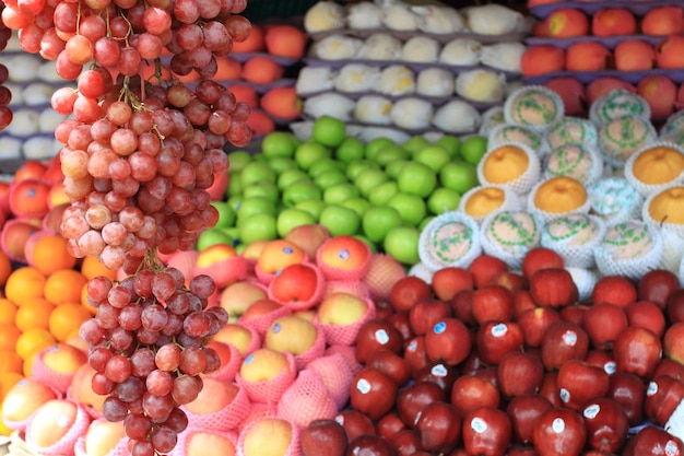 Bando de uvas vermelhas frescas penduradas e frutas coloridas embaçadas no fundo