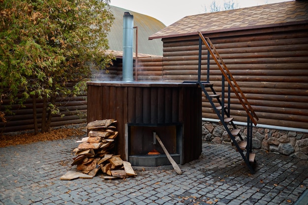 Bañera de vapor de madera con estufa y escalera en la terraza exterior en el patio. Procedimiento de spa e higiene