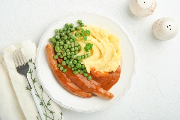 Bangers and mash Gegrillte Würstchen mit Kartoffelpüree und grünen Erbsen auf weißem Teller auf hellem Hintergrund Traditionelles Gericht aus Großbritannien und Irland BBQ-Rinderwürste Draufsicht