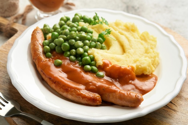 Bangers and mash Salsichas grelhadas com purê de batata e ervilha verde na chapa branca sobre fundo cinza Prato tradicional da Grã-Bretanha e Irlanda Salsichas de churrasco Vista superior