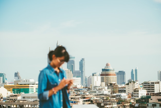 Bangkok-Stadtbildszene mit undeutlicher Frau benutzte intelligentes Telefon im Vordergrund mit Kopienraum