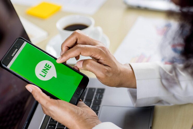 Foto bangkok/tailandia - 06 de agosto de 2021: empresarios sentados en la oficina trabajando con la computadora, sosteniendo sistemas operativos de teléfonos inteligentes con logotipos de la aplicación line, una de las aplicaciones de mensajería más populares.