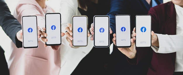 Bangkok / Tailândia - 06 de agosto de 2021: As pessoas seguram smartphones de diferentes marcas e vários sistemas operacionais com logotipos do Facebook, os aplicativos de rede social mais populares.