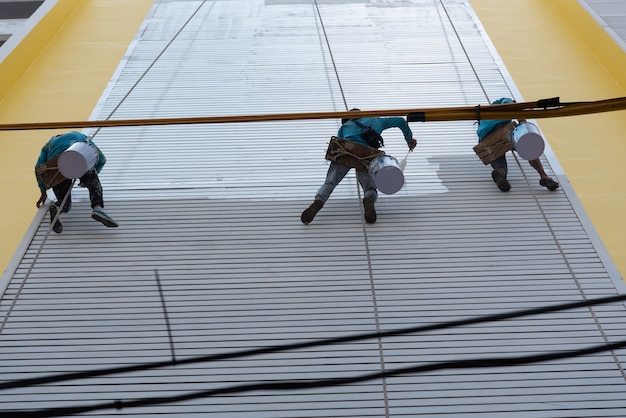 Bangkok, Tailândia - 23 de abril de 2017: pintor de construção asiático não identificado estava escalando o prédio por uma corda com segurança para pintar na parede para manutenção, renovação ou reparo