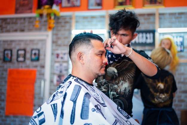 Bangkok, Tailandia - 25 de abril de 2017: Peluquero de hombre asiático no identificado o corte de pelo peinado un cliente de cuerpo regordete de hombre en peinado de moda en peluquería