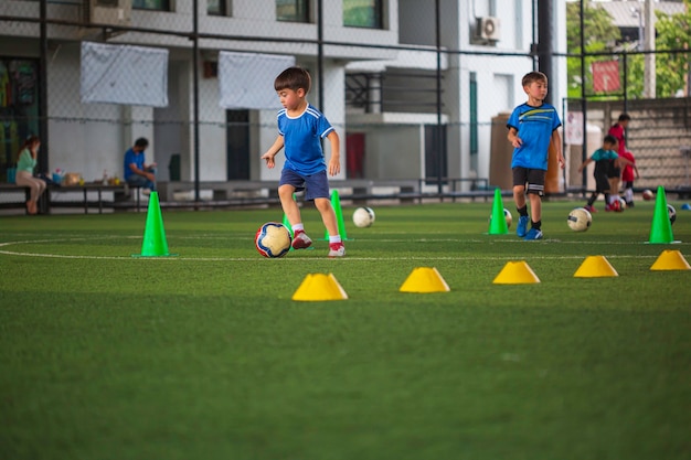 Bangkok - Tailândia NOVEMBRO-10, 2021 Crianças de táticas de bola de futebol controlam a bola em um campo de grama com cone para treinar Tailândia em treinamento de fundo em uma academia de futebol.