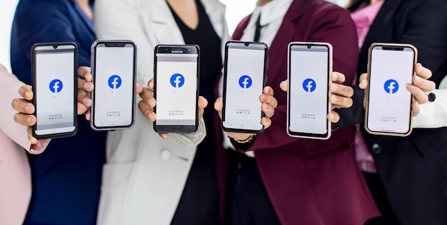 Bangkok/Thailand - 06. August 2021: Menschen halten Smartphones verschiedener Marken und verschiedener Betriebssysteme mit Logos von Facebook, den beliebtesten Anwendungen für soziale Netzwerke.