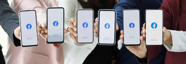 Bangkok/Thailand - 06. August 2021: Menschen halten Smartphones verschiedener Marken und verschiedener Betriebssysteme mit Logos von Facebook, den beliebtesten Social-Network-Anwendungen.