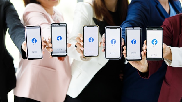 Bangkok/Thailand - 06. August 2021: Menschen halten Smartphones verschiedener Marken und verschiedener Betriebssysteme mit Logos von Facebook, den beliebtesten Social-Network-Anwendungen.