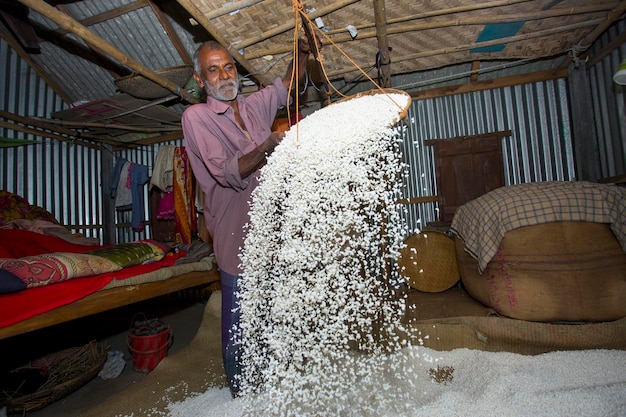 Foto bangladesh 09 de fevereiro de 2018 um trabalhador mais velho medindo prepara arroz tufado khoi de arroz glutinoso de casca de binni dhan como refeições tradicionais do festival bengali39s em savar dhaka
