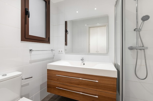 Banheiro com lavatório em bancada de madeira de lei com duas gavetas para produtos de higiene paredes com branco brilhante